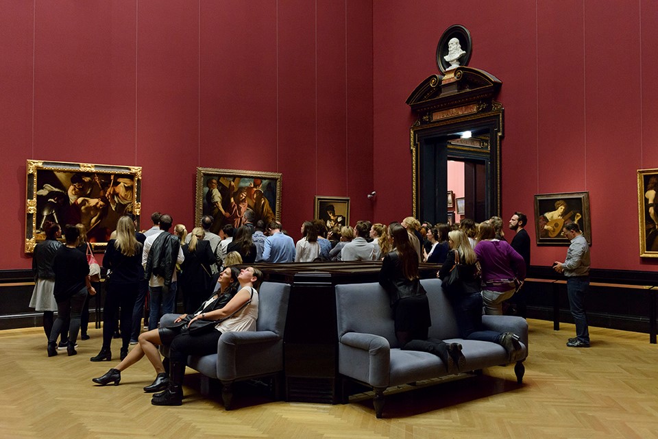 Besucher:innen einer Galerie betrachten Bilder an den Wänden und an der Decke